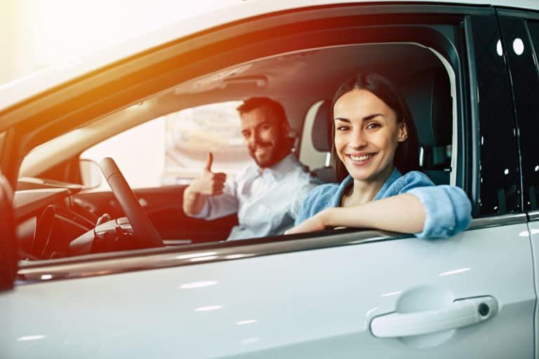 Happy smiling young couple chooses and buying a new car for the family in the dealership in sunlight.